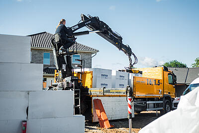 Ein LKW von JACOB CEMENT BAUSTOFFE entlädt mithilfe des integrierten Ladekrans eine Palette Kalksandsteine auf einer Baustelle