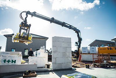 Ein LKW von JACOB CEMENT BAUSTOFFE entlädt mithilfe des integrierten Ladekrans eine Palette Kalksandstein passgenau in den Rohbau auf einer Baustelle