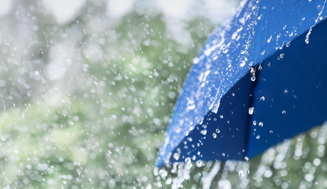 Ein blauer Regenschirm vor verschwommenem Hintergrund, auf den Regen prasselt.