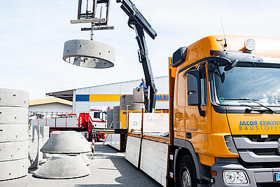 Ein LKW von JACOC CEMENT BAUSTOFFE lädt Schachtringe auf einer Baustelle ab